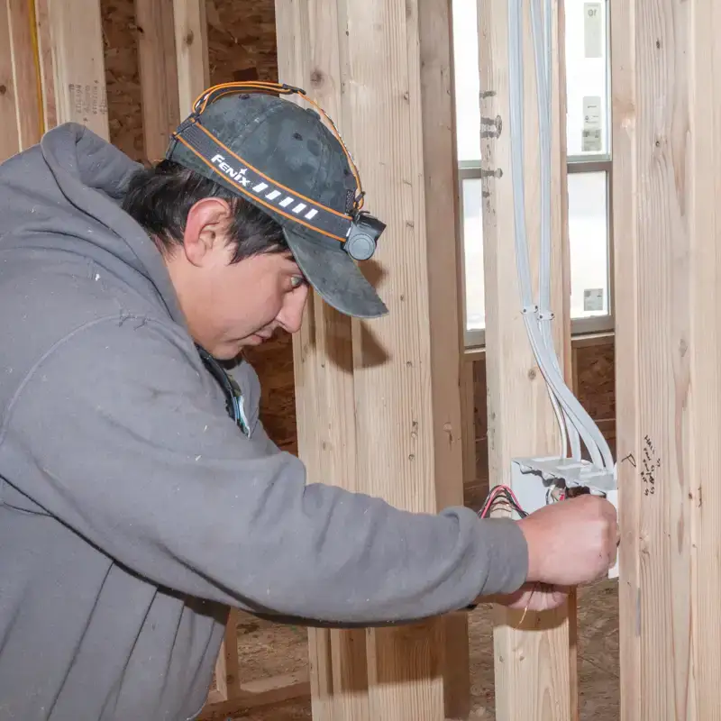 Electrician installing light switch in a new residential house build with bare wood framing.